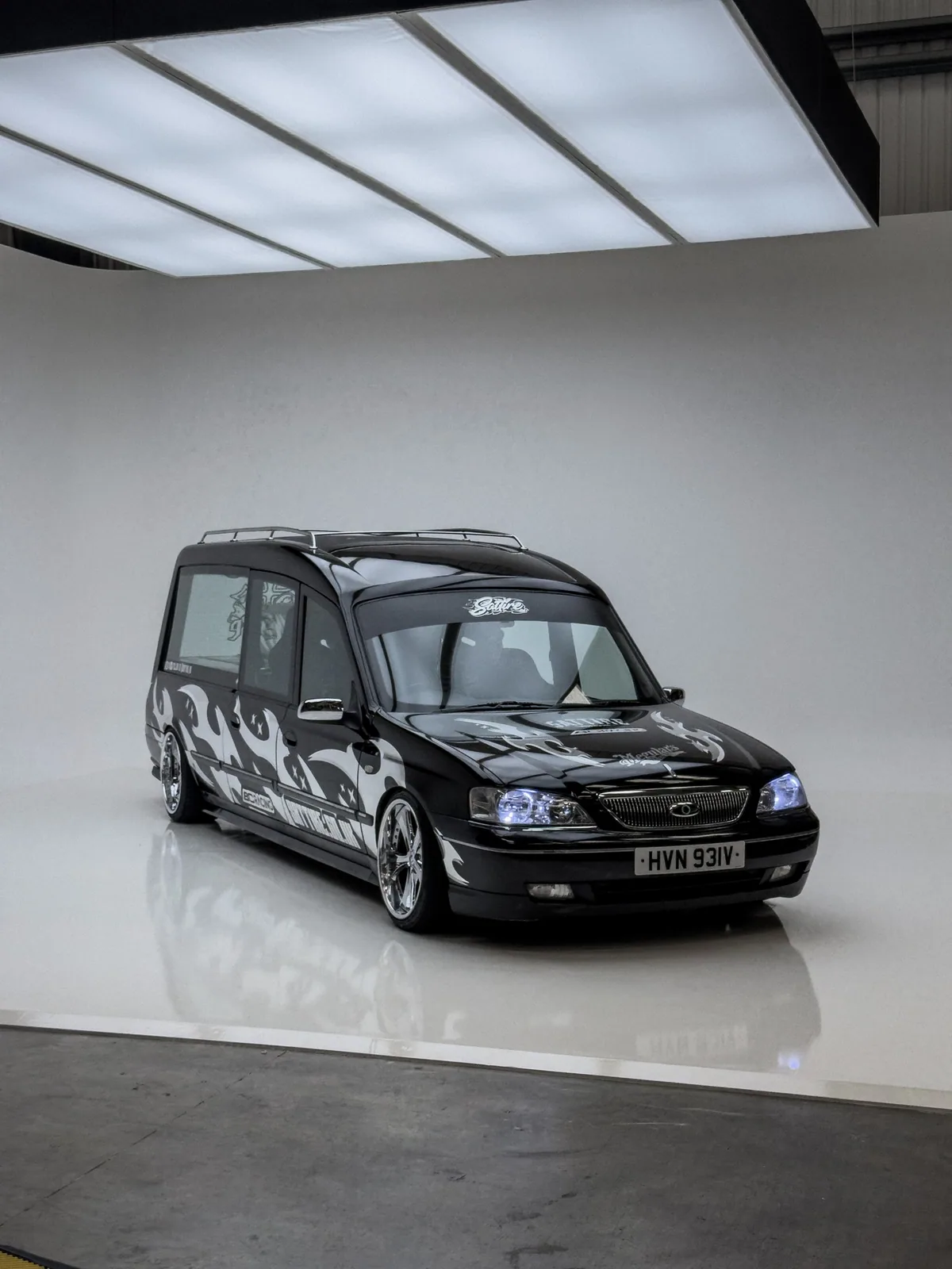 The SATTIRE hearse, a black Ford hearse on split chrome wheels with silver flame graphics, lit in a white studio